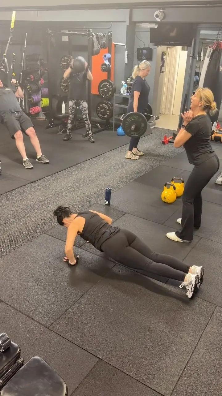 A small group class in the gym, one member doing press-ups while others lift